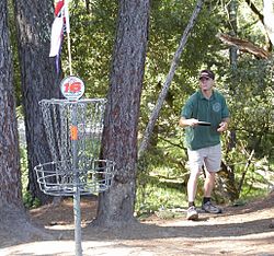 Man playing disc golf Disc golfer and basket.jpg