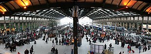 Vue panoramique du hall principal sous sa verrière, avec des TGV à quai.