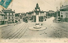 Carte postale ancienne montrant le carrefour de la Demi-Lune avec son horloge récemment érigée, au pied de laquelle se trouve une station du tramway de l'OTL