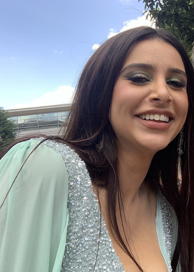 Woman with dark brown hair wearing a mint green dress and matching eyeshadow smiling.