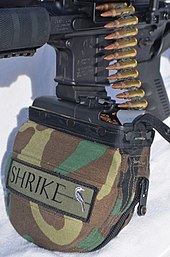 A 200-round M249 ammunition belt pouch attached to an Ares Shrike 5.56 via a magazine well adapter block Shrike 5.56mm Belt Fed Upper Receiver.jpeg