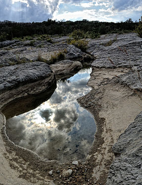 A small pool of river water reflects the big Texas sky