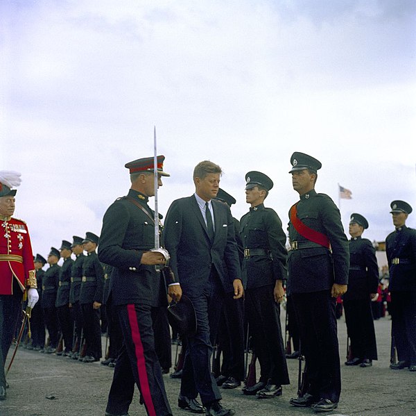 John Fitzgerald Kennedy, escorted by a Bermuda Militia Artillery officer in Royal Artillery blue No. 1 Dress, inspects green-uniformed riflemen of the