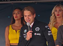 Augusto Farfus hablando a una audiencia en una pista de carreras con dos mujeres adultas detrás de él en 2018