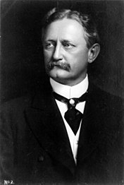 Portrait en noir et blanc d'un homme moustachu portant un costume