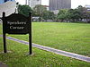 A brown wooden sign with the words "Speakers' Corner" in white next to a grassy field.