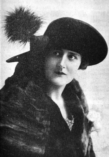 A white woman wearing a large black hat and a fur wrap