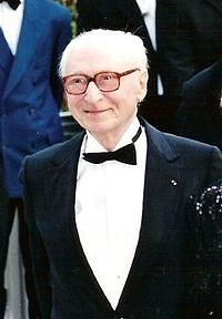 Photographie d'un homme âgé, aux cheveux blancs, portant des lunettes, en smoking, un sourire doux