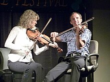 Natalie MacMaster and Donnell Leahy fiddle on stage while sitting in chairs