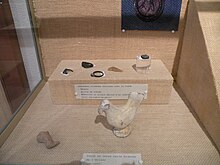 Photographie en couleurs d'objets dans une vitrine, dont une statuette en terre représentant une poule.