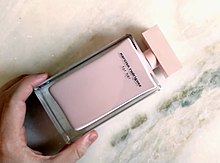 Photograph of a hand holding a rectangular pink bottle of perfume labeled Narciso Rodriguez for Her