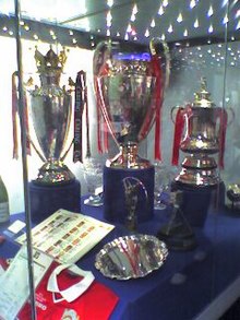 Three silver trophies on blue plinths in a glass display case.