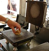 A ball of dough is placed on a waffle iron to make the waffle for a stroopwafel.