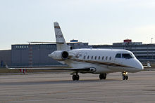 A small white jet aircraft, with two jet engines on its tail, on the tarmac