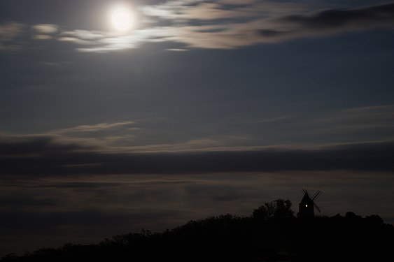 The moon rising above the dark silhouette of a windmill