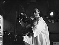 A baby is baptized by a chaplain on a Royal Navy armed trawler in 1943.