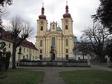 Kamenná zídka, před níž stojí kašna. V pozadí kostel Nanebevzetí Panny Marie a vlevo je patrný objekt kláštera.