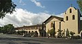 Photograph of Mission Santa Inés, showing the campanile on the right, the chapel at center, and the long, colonnaded walkway to the left.