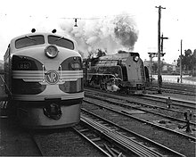 Locomotive diesel à nez rond se trouve à côté d'une locomotive à vapeur simplifiée de la classe S.  (Image en noir et blanc)