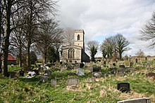 A stone church from the east seen at a distance in a churchyard, showing the east window and a battlemented west tower