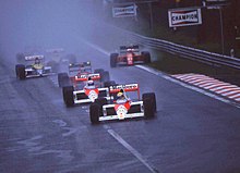 Photo de plusieurs monoplaces en formation rapprochée. Senna est en tête suivi de Prost (F1 rouges et blanches), Berger, Boutsen et Mansell (avec deux roues dans l'herbe).