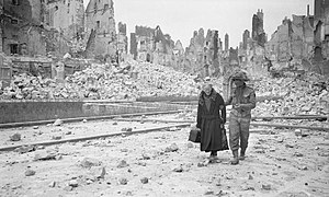 Un soldat britannique aide une vieille femme à marcher dans les décombres de Caen.