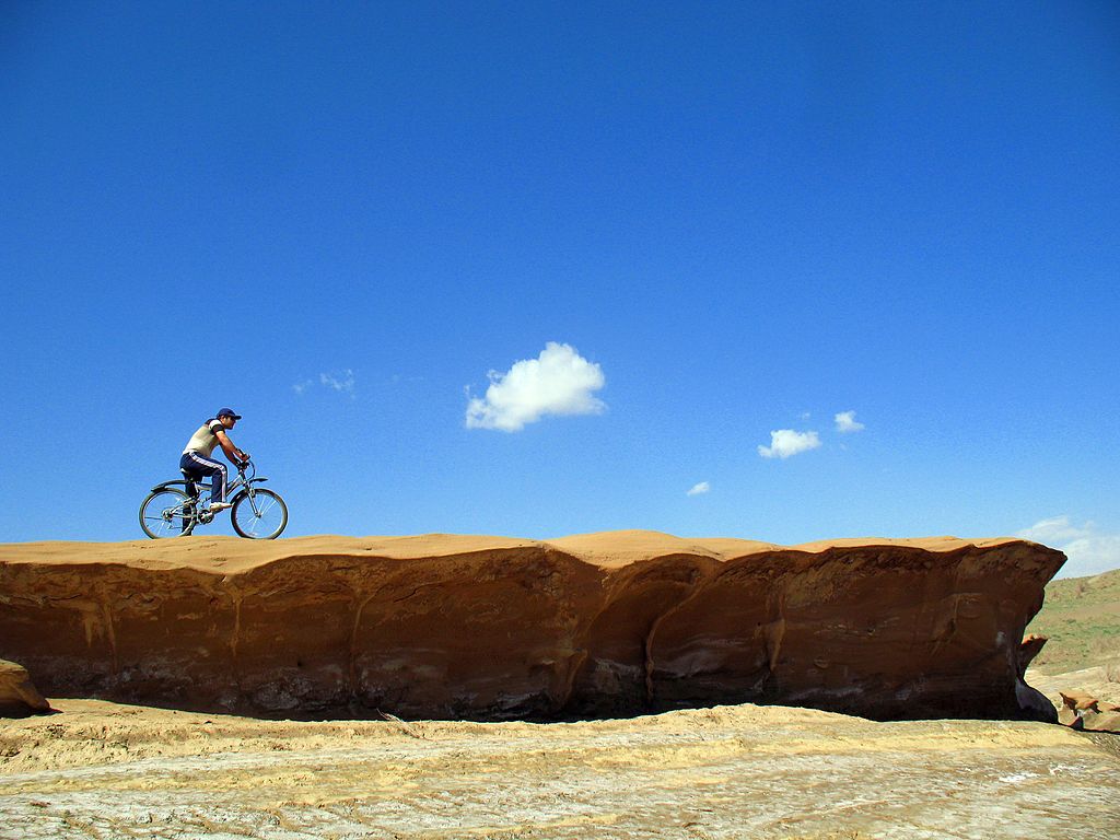 una persona andando en bicicleta sobre tierra color rojo naranja con el cielo azul