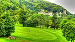 a golf course, in the background is the top of a castellated mansion can be seen within the woodland