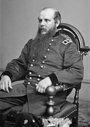 Black and white photo of a seated man in a dark military uniform with two stars on his shoulder tabs. He is balding and has a long beard.