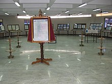 Photo couleur d'une salle contenant de nombreux manuscrits et photographies sous verre ; au centre, un piédestal exhibant une biographie de Ramanujan, sous une statuette le représentant.