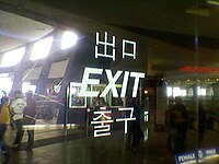 Багатомовний знак на виході із супермаркету SM Mall of Asia[en] у місті Пасай, що у Філіппінах. верхній напис «Вихід» читається як японською, так і китайською (deguchi та chūkǒu відповідно). Далі йде текст англійською та корейською (chulgu). Хоч англійська мова була розповсюджена на Філіппінах, відтоді як країна була територією США, філіппінці пристосовуються до збільшення кількости мігрантів та туристів.