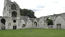 Deux pans de murs portant des arcs formerets au centre d'une pelouse et surmontés de l'abbatiale