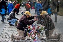 A National Park Service volunteer kneels and uses paper and a graphite stick to create a rubbing of a name from the Vietnam Veterans Memorial. Volunteers obtain name rubbings, Vietnam Veterans Memorial (39709b23-daff-4632-86a1-2bf7e1e534d1).jpg