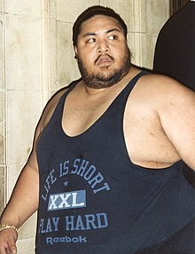 Un homme obèse portant un marcel bleu foncé.