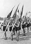 HJ-ungdom på utmarsj under Rikspartidagene i Nürnberg på 1930-tallet, nazistpartiets årlige massemønstring. Uniformene består av brune skjorter, svarte speidertørkler, båtluer og kortbukser samt HJs armbind med hakekors i hvit rute. Foto: Deutsches Bundesarchiv