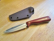 Fixed-blade knife with wooden handle on a table, next to a molded plastic sheath