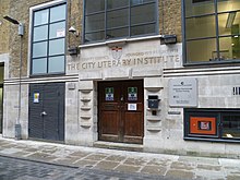 This was originally an entrance, as indicated by the carved name of the building, but the opening is now only used as a fire exit (London). City Lit fire exit London.JPG