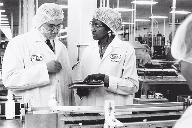 Inspección de una fábrica de medicamentos en Baltimore, a principios de la década de 1990.  Kirk Sooter y Sarah Brown examinan los registros de lotes de productos cuando estos llegan a la línea de llenado.