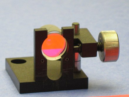 A dielectric mirror used in tunable lasers. With a center wavelength of 600 nm and bandwidth of 100 nm, the coating is totally reflective to the orange construction paper, but only reflects the reddish hues from the blue paper.