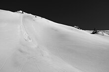 Fotografie laviny z volného sněhu. Ta začíná v jednom bodě horním levém rohu fotografie pod malým smrkem a trojúhelníkovitě se rozšiřuje směrem dolů.