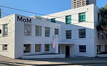 Fotografie muzea muzeí, bílá budova s ​​malovaným nápisem „MoM“.