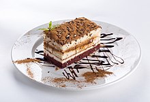 Piece of chocolate cake on a white plate decorated with chocolate sauce.jpg