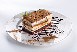 Part de gâteau au chocolat, saupoudrée de poudre de cacao, sur une assiette blanche décorée de sauce au chocolat.