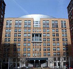 View of Stuyvesant High School's façade from about a quarter-mile away. Most of the facade is orange brick, but the three-story entrance way at the center of the image is made of metal.