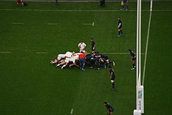 Vue des tribunes d'une mêlée proche de l'embut des joueurs en bleu.