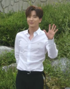 Leeteuk smiling with his left hand raised in greeting, palm facing outwards