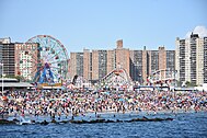 Überfüllter Strand von Coney Island mit Riesenrad und Achterbahn im Hintergrund