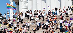 Människor står på trapporna av katedralen i Helsinki och firar Pride-festivalen med färgglada flaggor och dekoration.