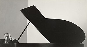 Stravinsky leunt met zijn arm tegen een vleugelpiano met het deksel omhoog