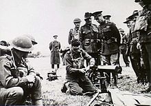 A blindfolded soldier demonstrates assembling a machine gun to onlooking officers